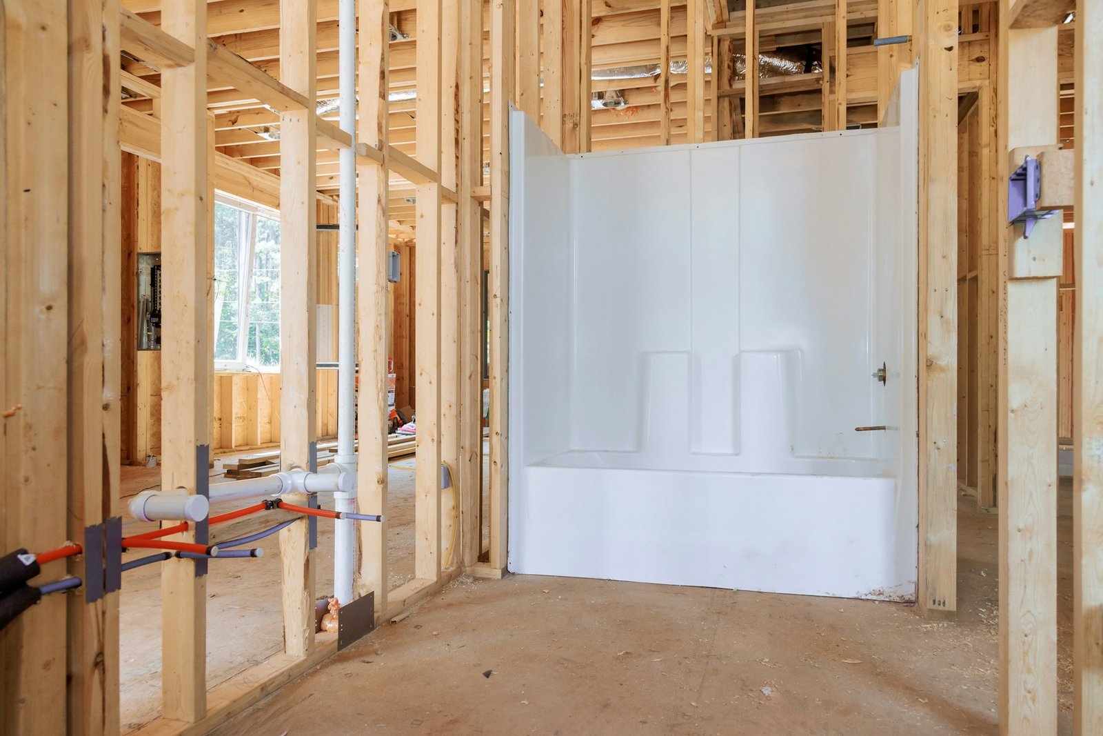 Newly added acrylic bathtub in under construction house bathroom amid beams frame